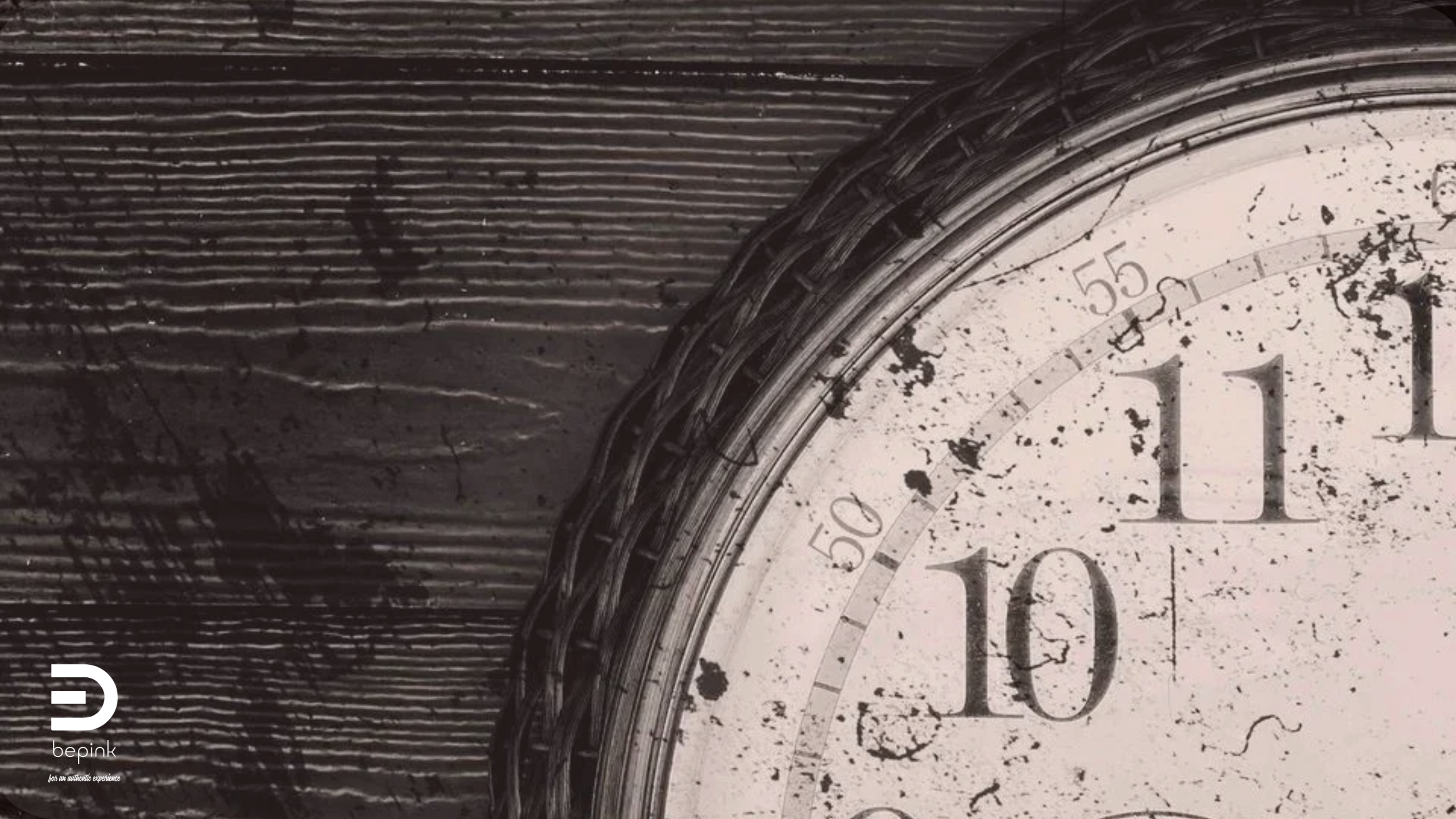Close-up of a vintage wall clock with worn Roman numerals, partially visible on the right side against a dark wooden background. The BePink logo appears in the lower left corner.