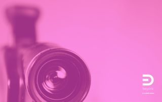 Obiettivo di una cinepresa in primo piano, trattato nei toni del magenta, simbolo di uno sguardo che osserva la realtà da una prospettiva diversa.